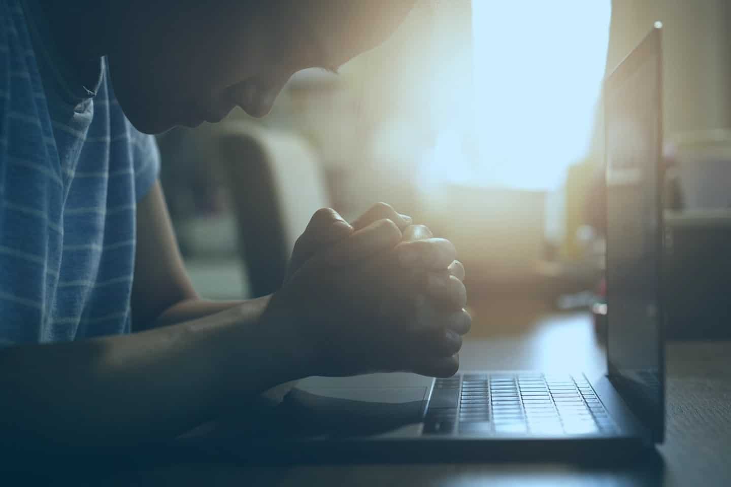 Man prays over laptop - church AV systems provided by Marshall Industries