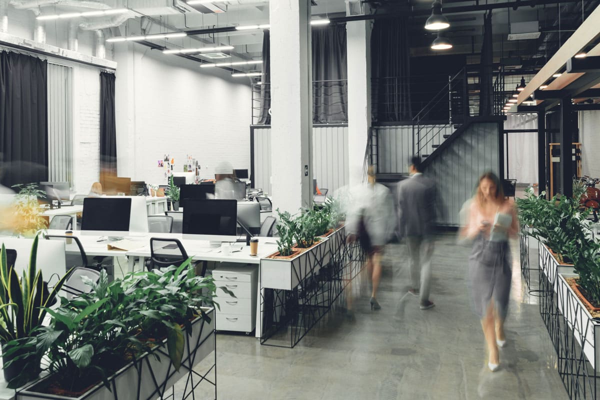 A timelapse compilation photo of an open-plan corporate office with employees walking through the office, illustrating the need for effective commercial sound systems