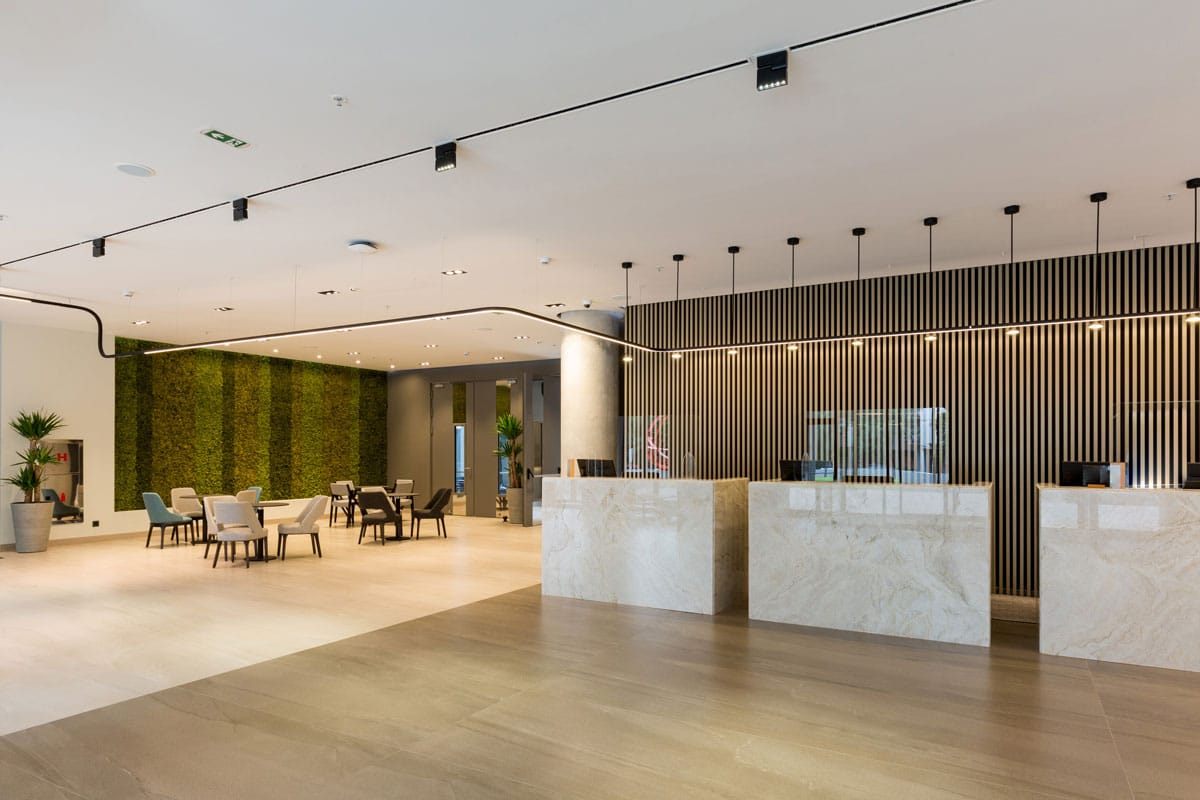 A lobby with front desks, a sitting area, and a grass wall. Installing a commercial sound system elevates the experience for retail and hospitality companies.