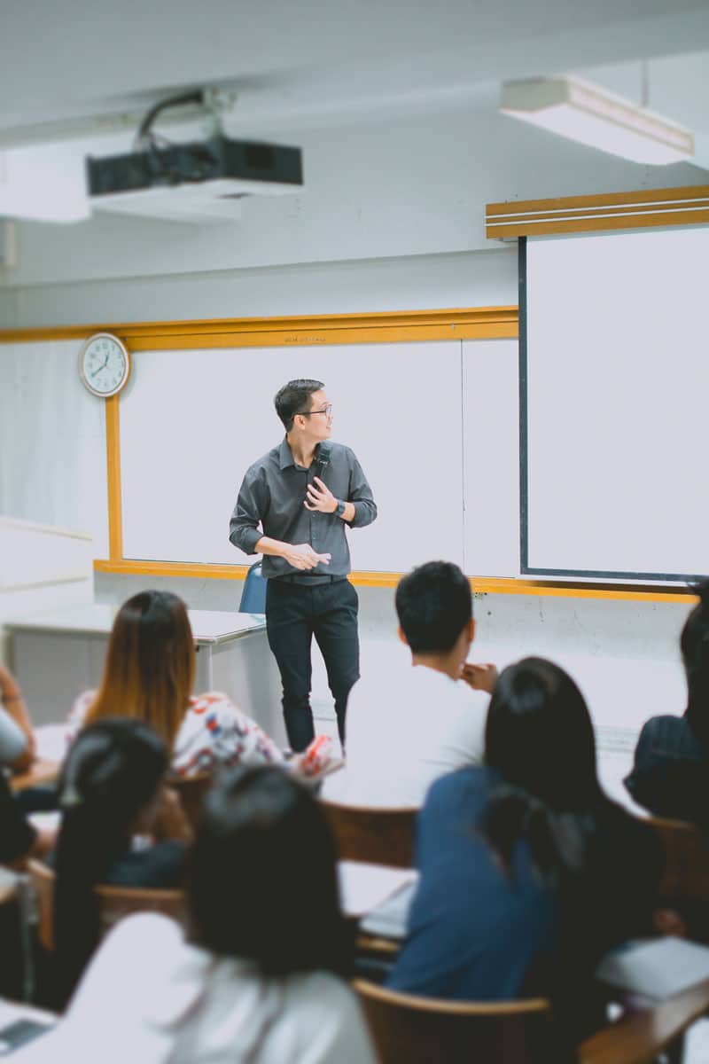 Teacher presenting to students in a classroom with a ceiling-mounted projector, the interactive display setup Marshall Industries builds into K-12 classrooms.